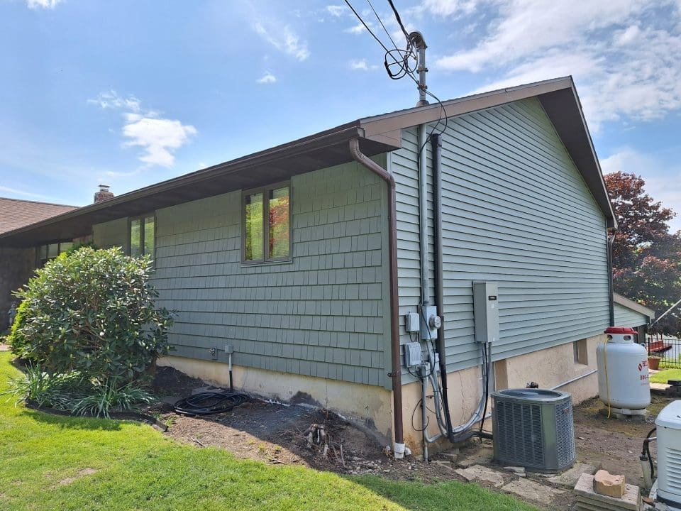 A view of the back corner of a house with blue-green siding materials.
